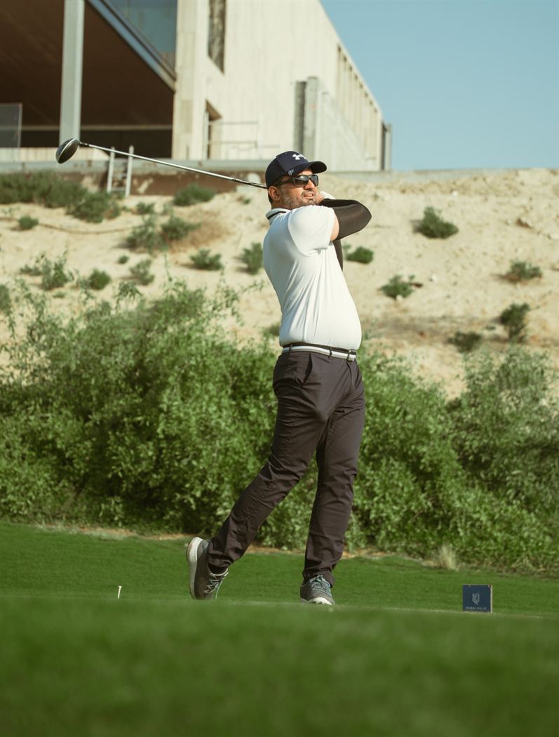 A member driving from a tee beside the desert at Dubai Hills Golf Club